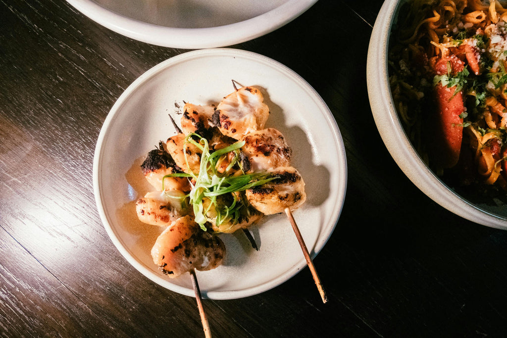 Skewered chicken with green onions on a white plate with a dark background