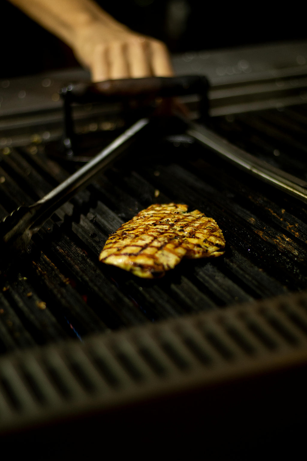 Grilled pineapple on a barbecue grill with tongs